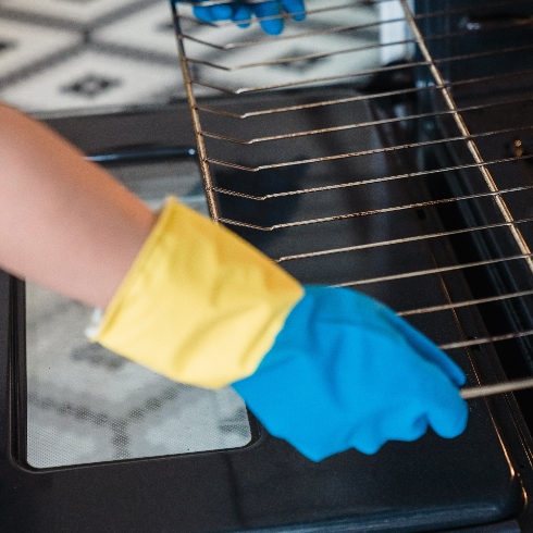 A person wearing rubber gloves while cleaning an oven