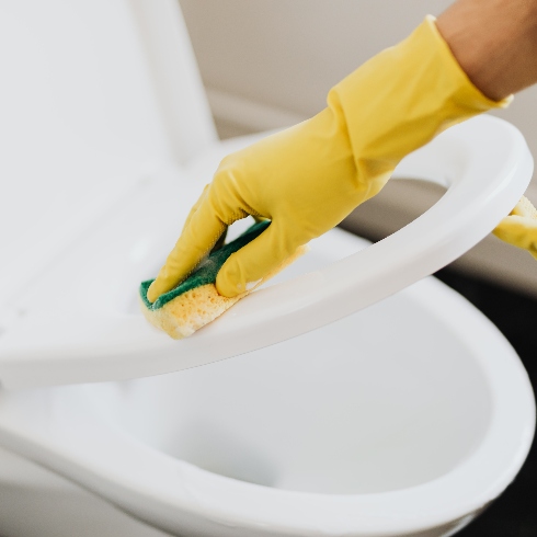 Someone wearing yellow rubber gloves scrubbing a white toilet