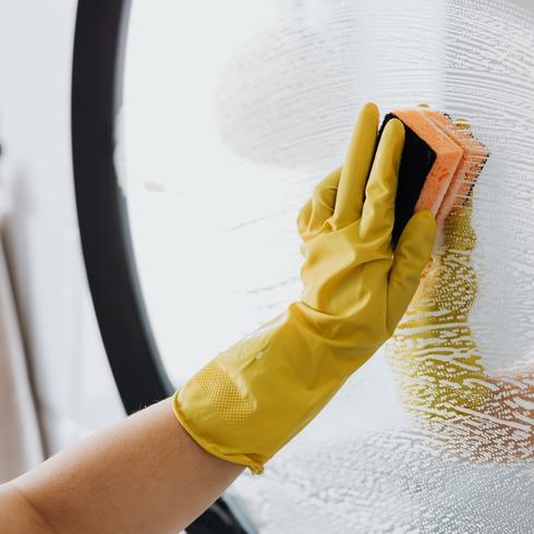 a person with yellow rubber gloves cleaning a mirror