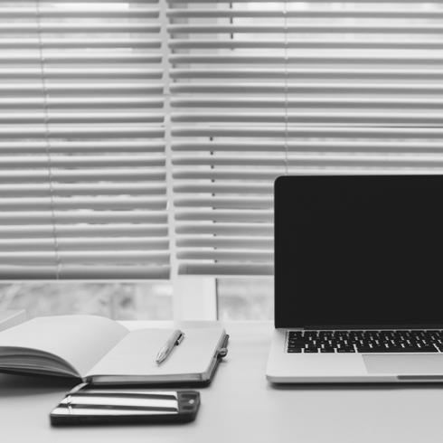 a notebook and a laptop on a white desk with blinds