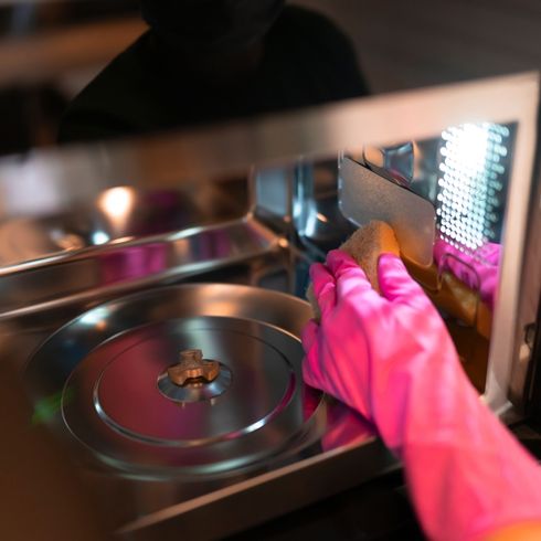 A person wearing pink rubber gloves, cleaning microwave.