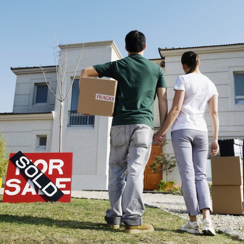 couple stands in front of white house with sale sign