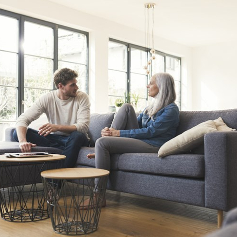 Man and mother sit on grey couch in front of window