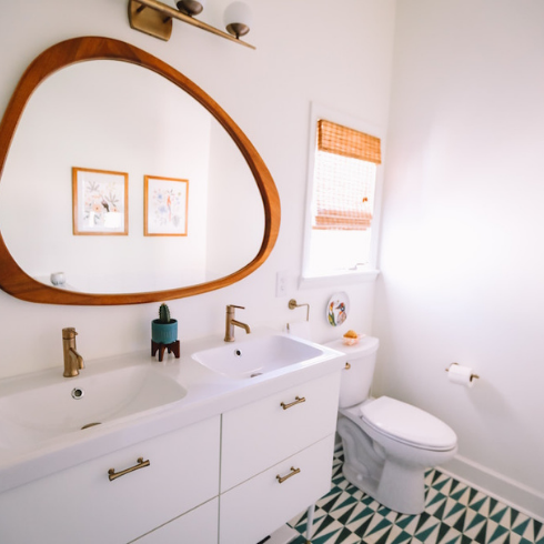 An all-white bathroom with a unusual mirror and minimal decor