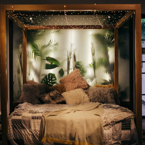 wood canopy bed with plush pillows in bedroom with plants behind frosted glass