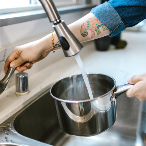 Person pouring water into a pot from the kitchen tap