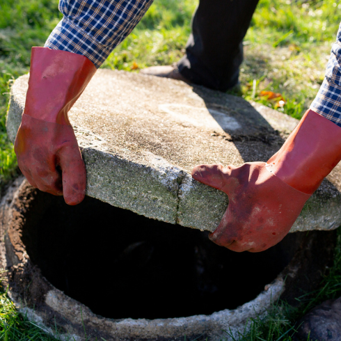 Plumber in gloves lifting up cover of septic tank