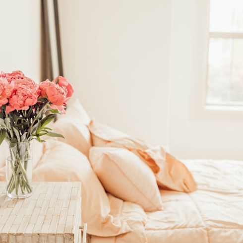 white bedroom with white bed and pink flowers on bedside table