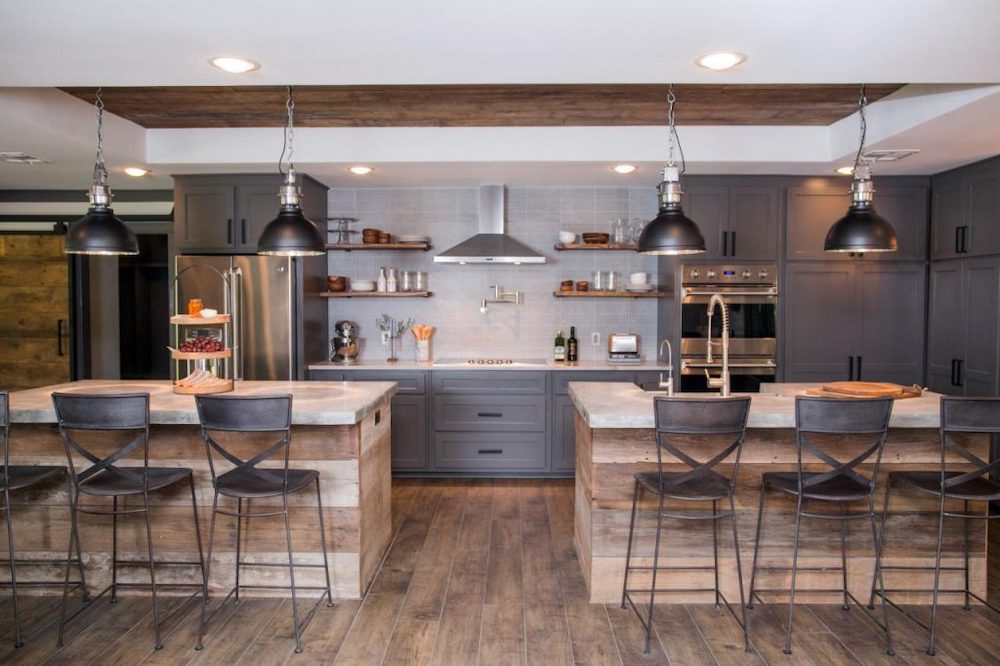 Matching wide plank islands anchor a large space, while darker cabinets and vintage lighting offer contemporary contrast mixing new and old, farmhouse and industrial