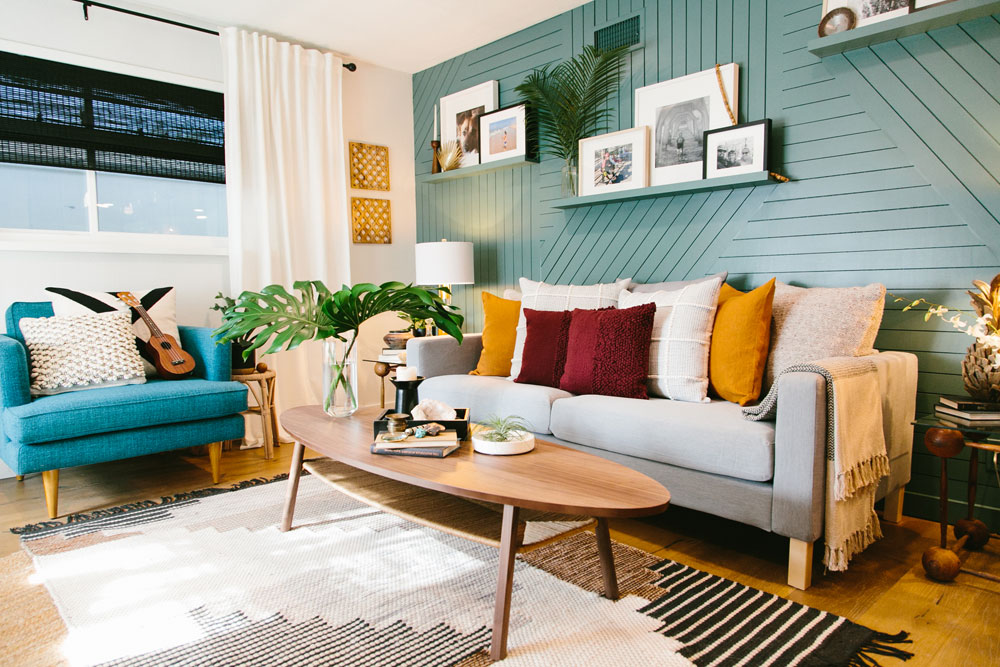 Deep aqua accent wall with a ridged treatment in a retro living room with funky carpets, jewel-tone pillows, mid-century modern furniture as featured on Home Network’s Hidden Potential