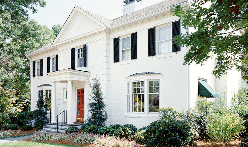 Exterior of a classic colonial house with black shutters painted in BEHR Carbon N520-7, the main house painted in BEHR Dusting Powder BL-W05 and the red door painted in BEHR Allure PPU2-03