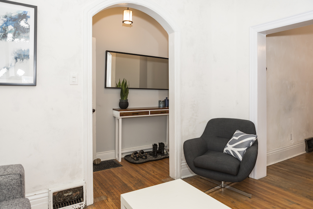 Grey egg chair in an old living room with antique wood floors and shoes in the hallway