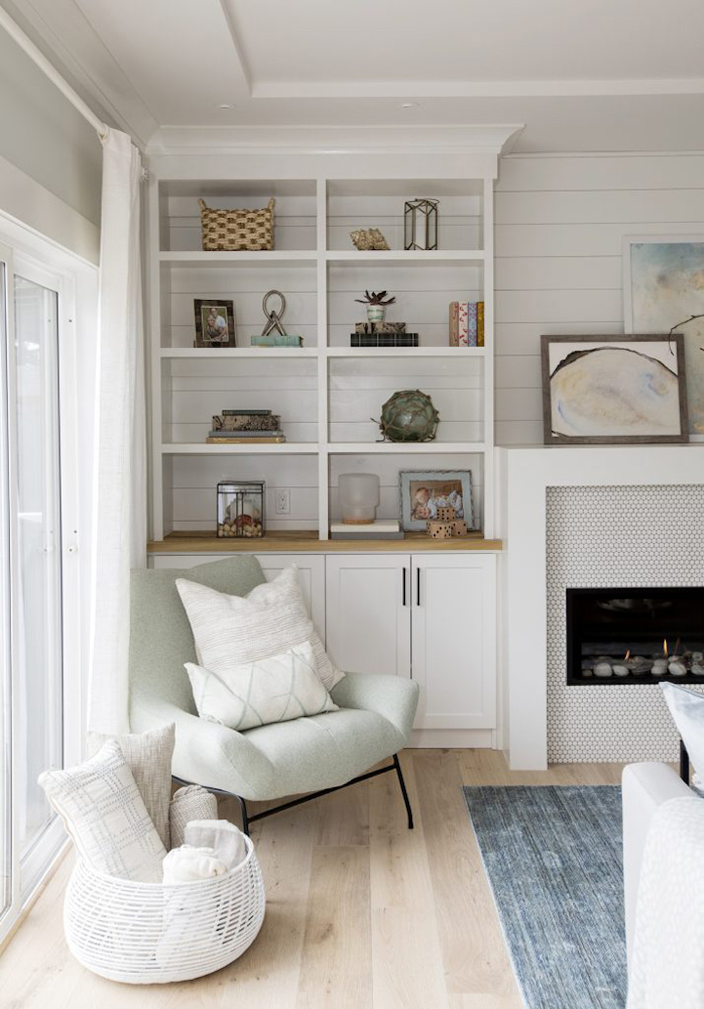 Beautifully curated bookshelves with a selection of photographs, candles, plants, art and mementos on a featured wall in an all-white living room featured on Home Network