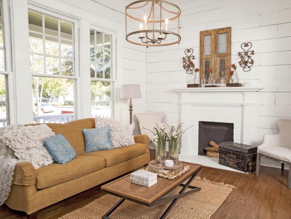 Shabby chic living room with white shiplap wall, mustard yellow couch, wood and metal coffee table, grass rug and gas fireplace