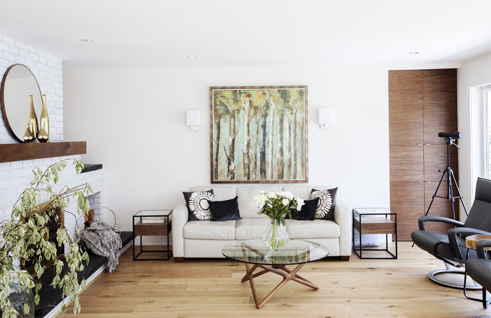 light sofa with black and white cushions, painting of trees and round glass top coffee table