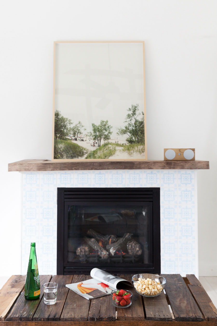 A wooden mantel, beachy artwork and subdued tiles gives this charming living room a serene feel.