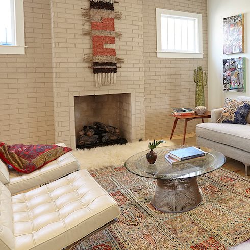 An eclectic living room decorated in the bohemian style with a woven wall hanging above the fireplace, a Persian rug on the floor, woven throw pillows on the taupe upholstered couch, two white leather reclining chairs, and BEHR Silky White PPU7-12 and Roman Plaster PPU7-10 painted on the walls