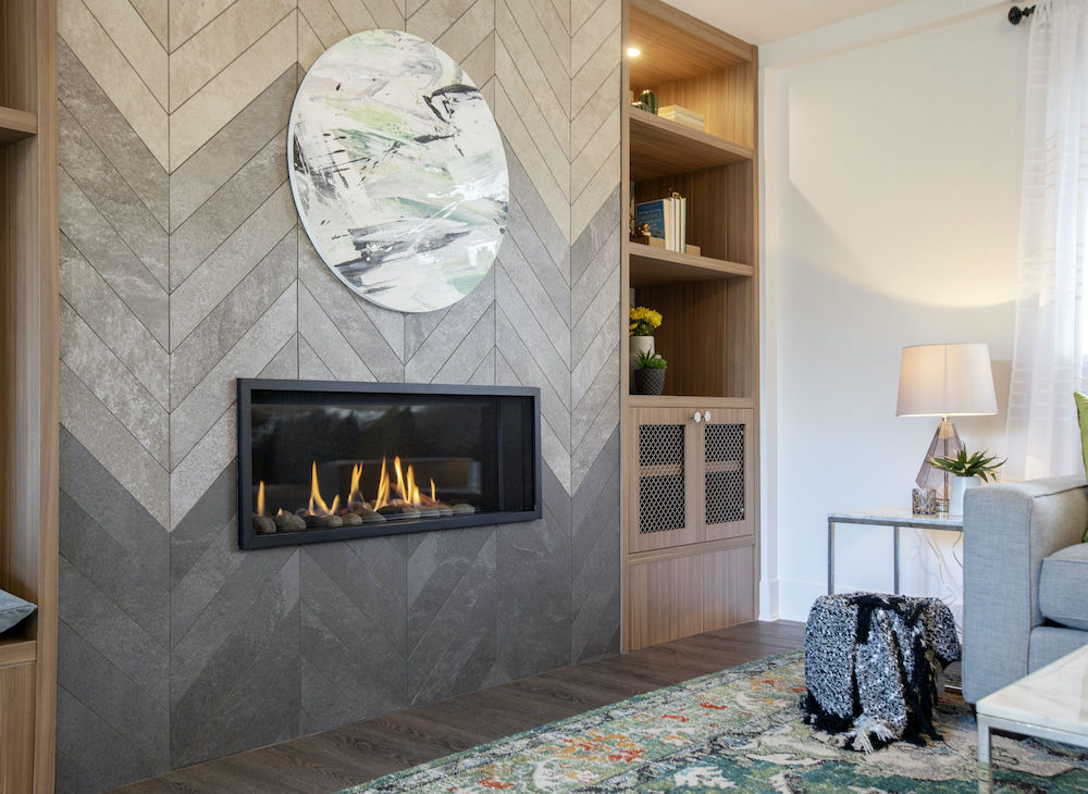 Chic living room with a long gas fireplace set into a feature wall with grey herringbone tile in an ombre pattern, dark wood floors, and built-in shelves as featured on Home Network’s Worst to First