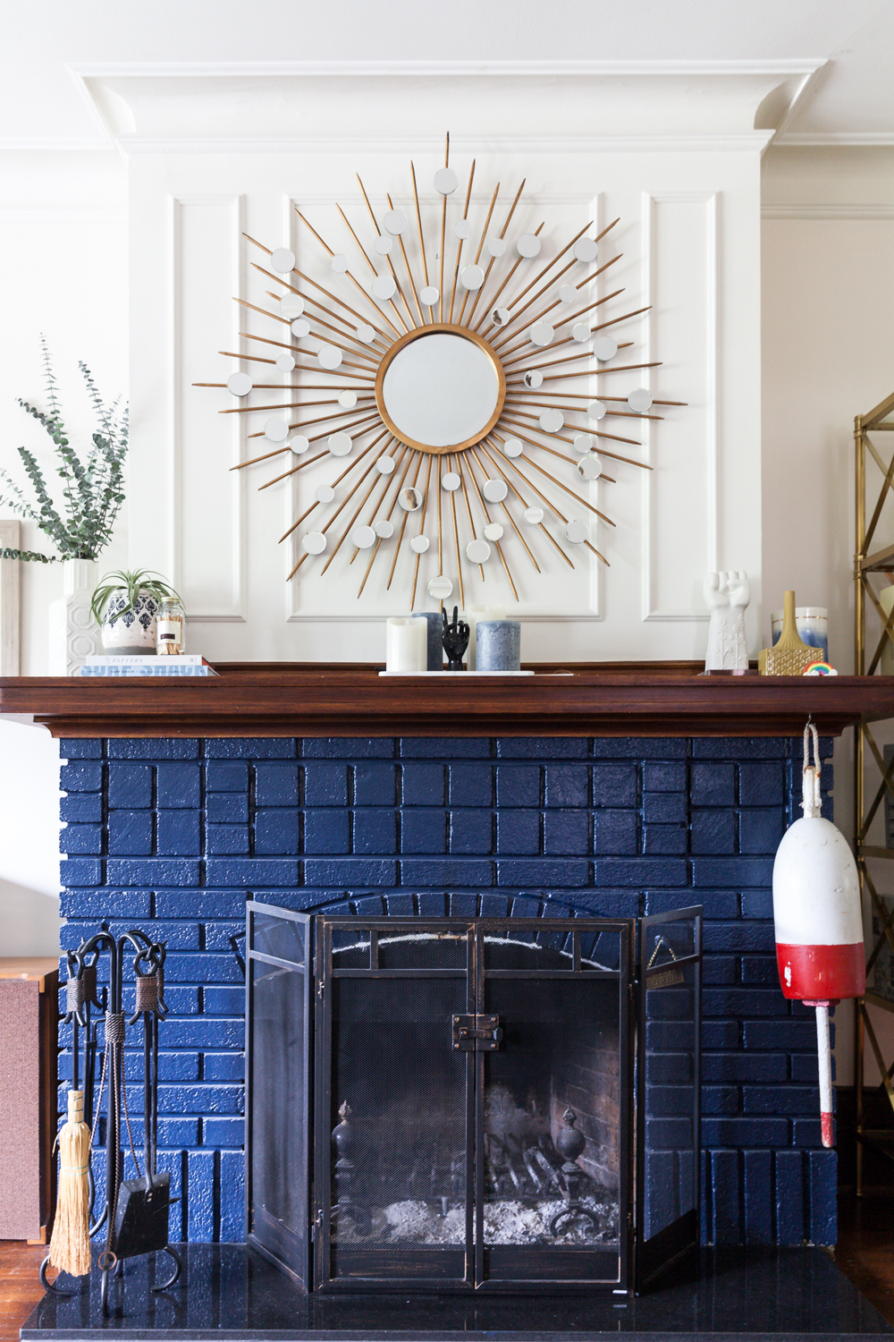 Retro fireplace design with blue-painted brick and vintage sunburst mirror above mantel.