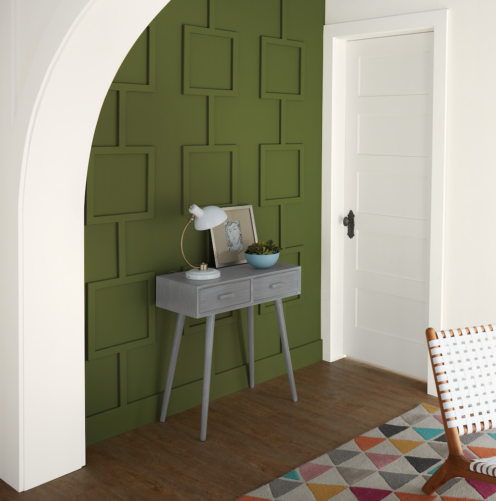 Striking entryway with a grey table with a blue succulent bowl, a white lamp, and framed artwork, dark wood floors, a colourful geometric rug, white door and archway paint in BEHR Ultra Pure White® and a paneled wall painted in BEHR Secret Meadow S360-6