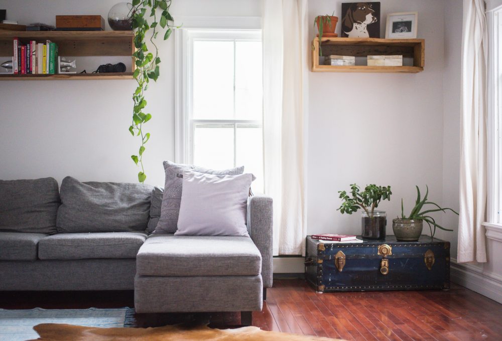 grey sectional in front of window beside blue trunk on floor