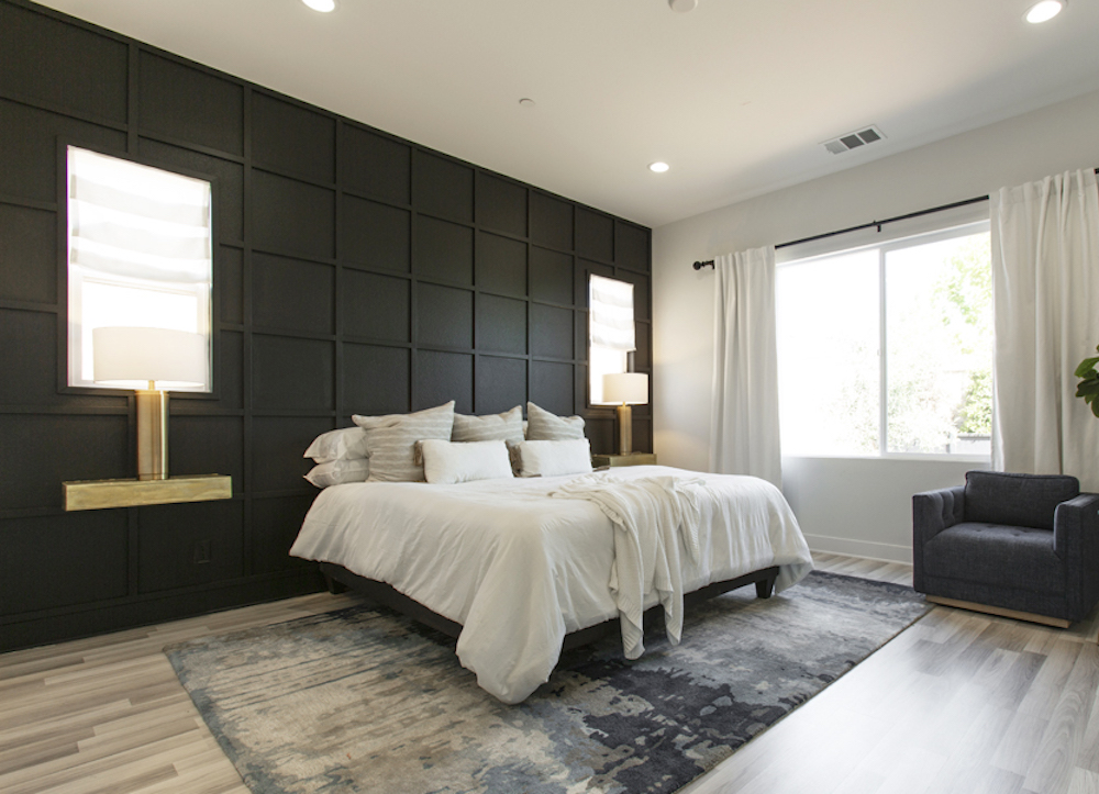 Chic bedroom with blonde hardwood, a large patterned area run, and a black panelled accent wall with built-in lamps and windows as featured on Boise Boys for Home Network