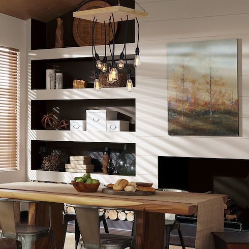 A chic industrial-inspired dining room features a long rough-edge wood table, four aluminum chairs, a black pendant light with many individual filament lightbulbs, a fireplace and walls painted in BEHR Spun Wool N220-1 and Off Broadway MQ1-35