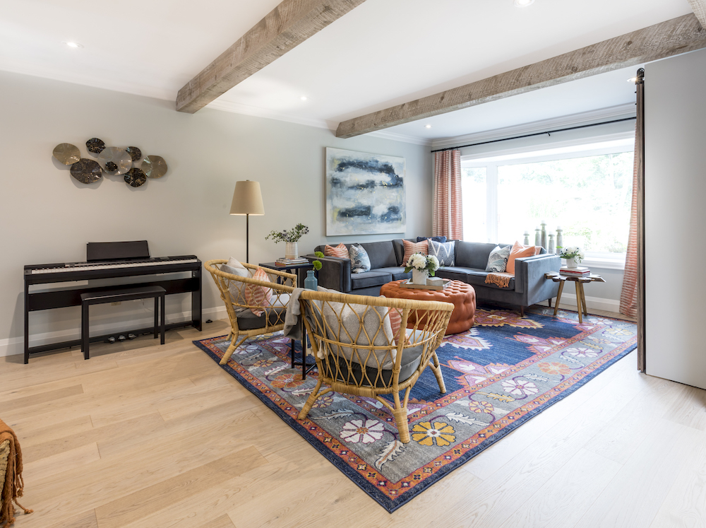 Newly renovated living room with rattan chairs and large blue sectional couch on a multicoloured rug