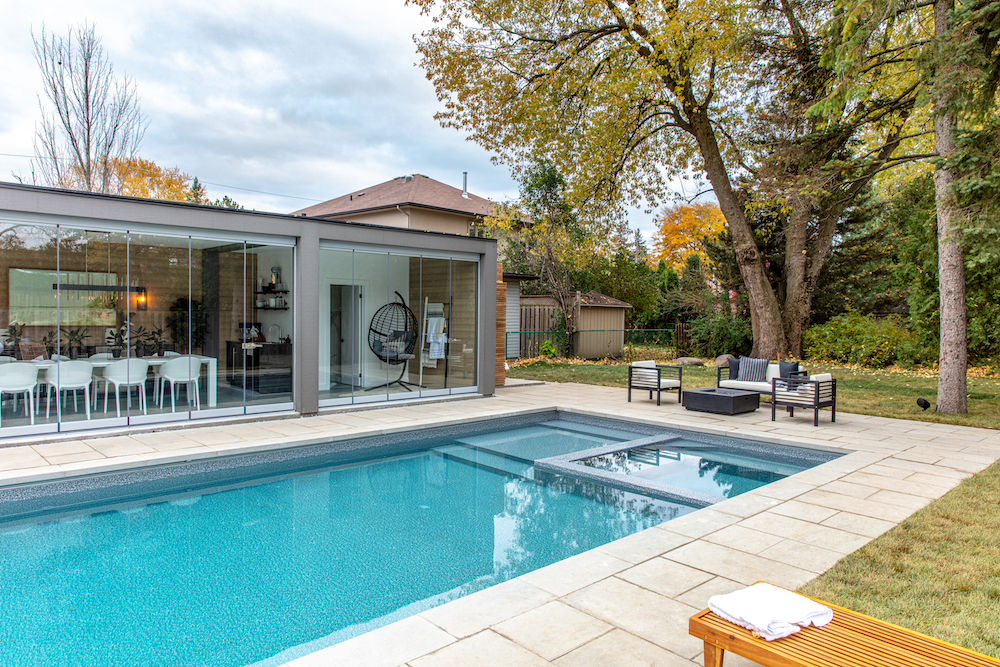 blue in-ground pool with adjacent firepit and glass-wall lanai