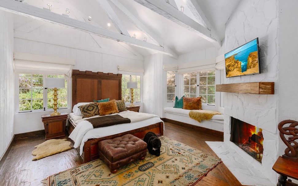 wooden bed in white bedroom with fireplace and wood floors