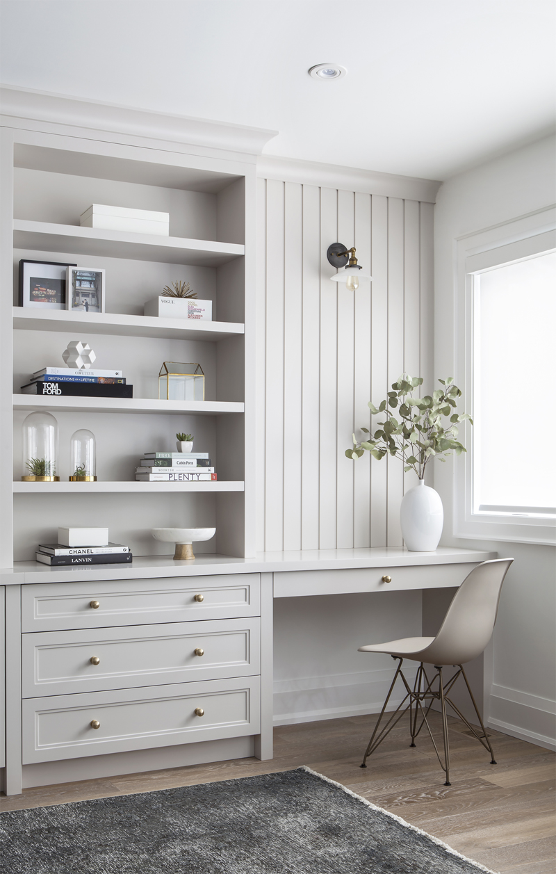 An airy living room with a nook for a desk and bookshelf with a sprig of eucalyptus in the corner of the desk