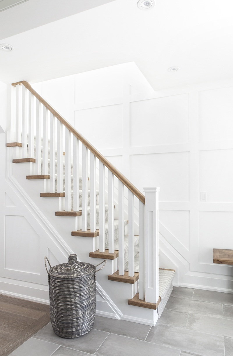 A neutral-toned entryway with a carpet runner on the staircase and grey floor tiles