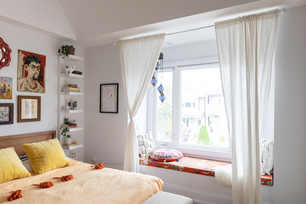 Yellow bed with gallery wall above and white floating shelves beside and window seat