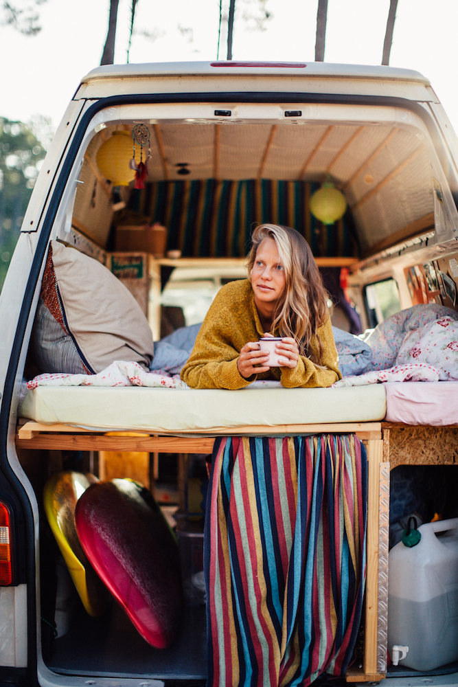 woman in camper van with striped curtains and surfboards