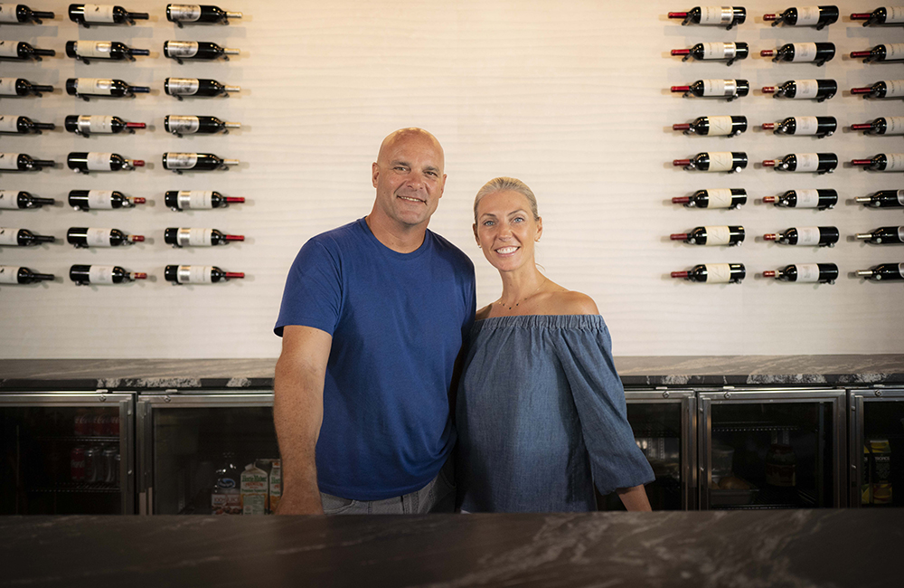 Bryand and Sarah Baeumler in front of a wall with wine bottles