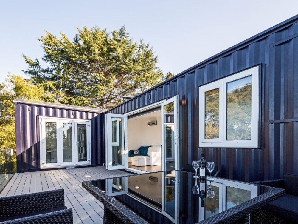 Eco-friendly navy blue storage container home with white trim and large wooden patio