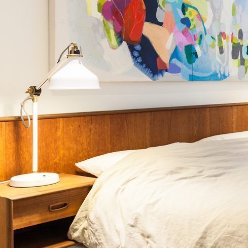 A white basement bedroom with pops of colour with the artwork and lamps