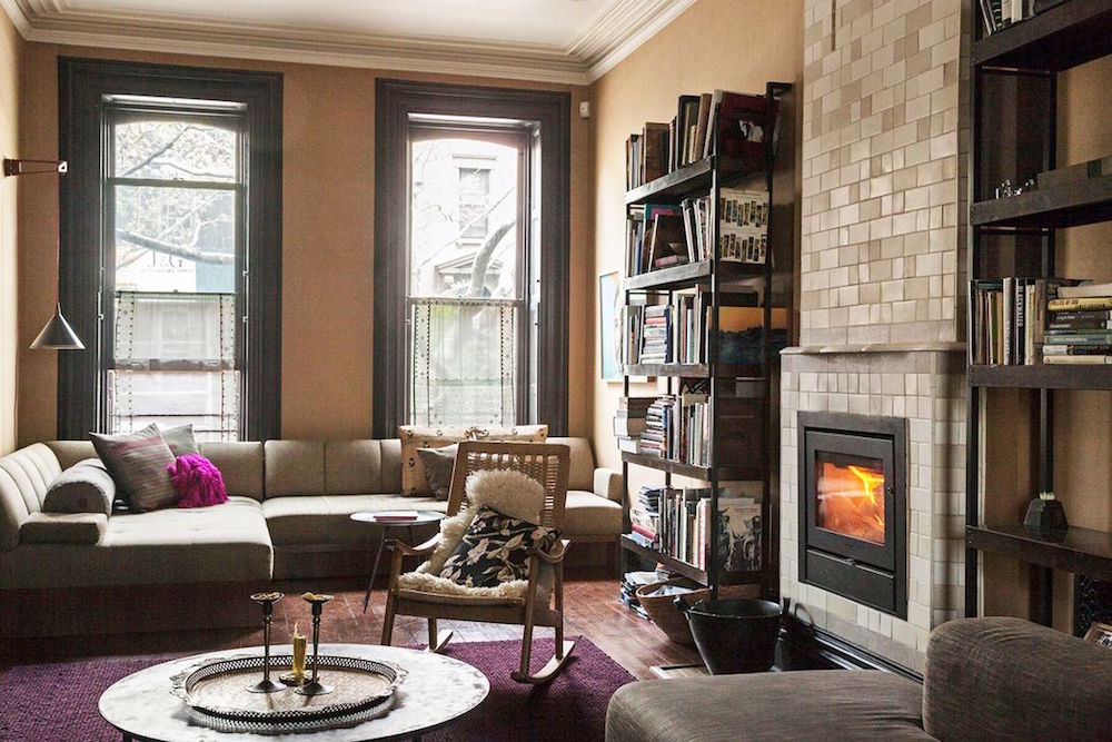 sectional couch, bookshelf and fire place in cozy living room with two windows