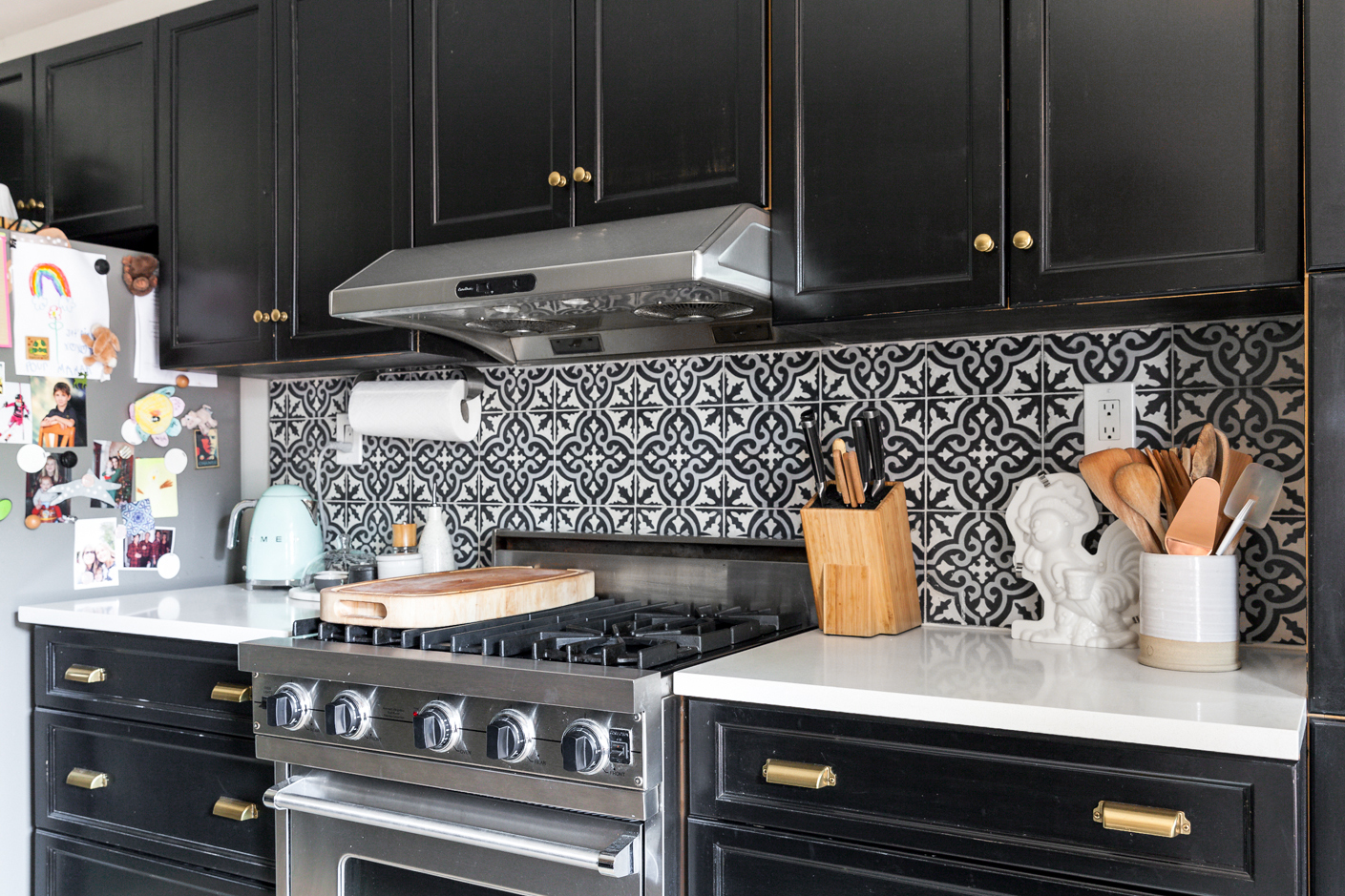 Black kitchen cabinets with brass pulls alongside encaustic-tiled backsplash.