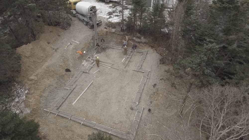 workers pouring foundation in forest lot