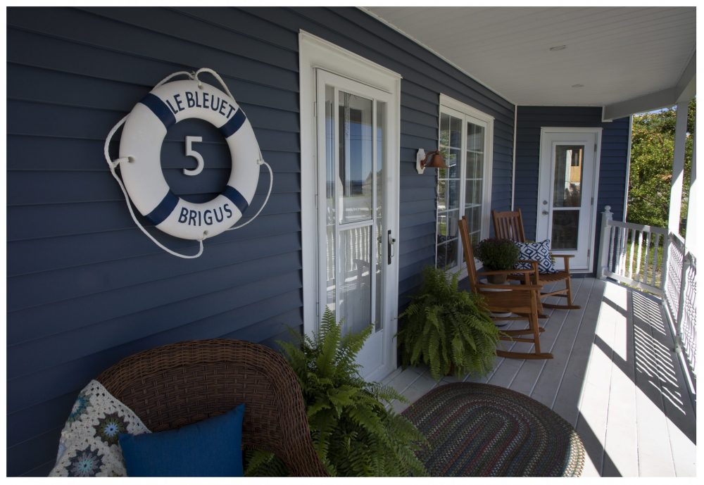 Blue house exterior with life saver decoration that says “Le Bleuet Brigus” and rocking chairs on the porch