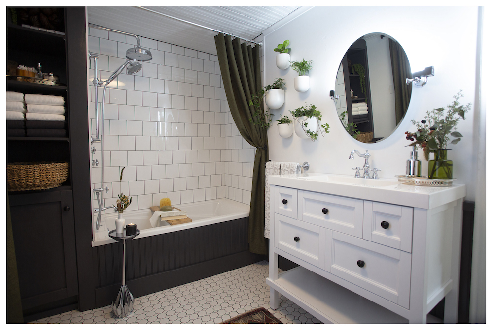 bright white bathroom with white vanity, round mirror and dark grey woodwork on tub surround