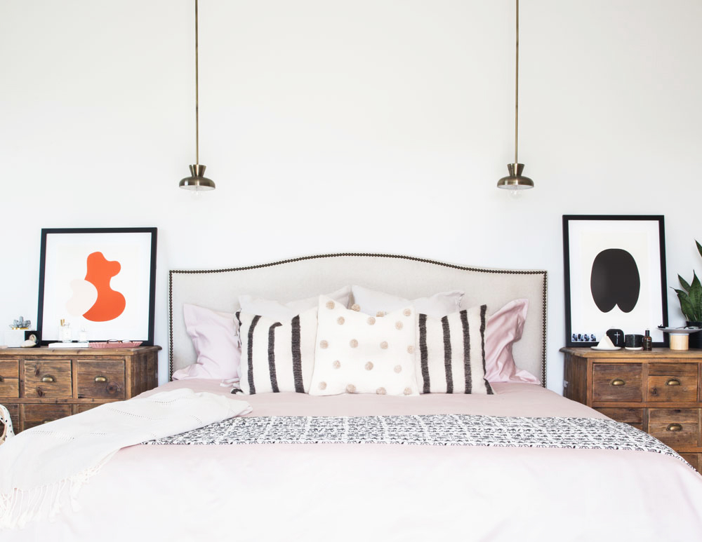 Two narrow light fixtures hang down above a bed centred between two nightstands on each side