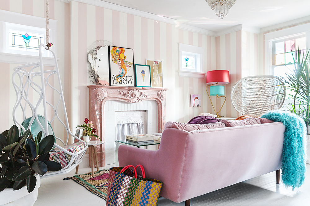 Colourful living room with pink-striped walls, a pale pink fireplace and pink velvet couch. Inside the fireplace is a white curtain.