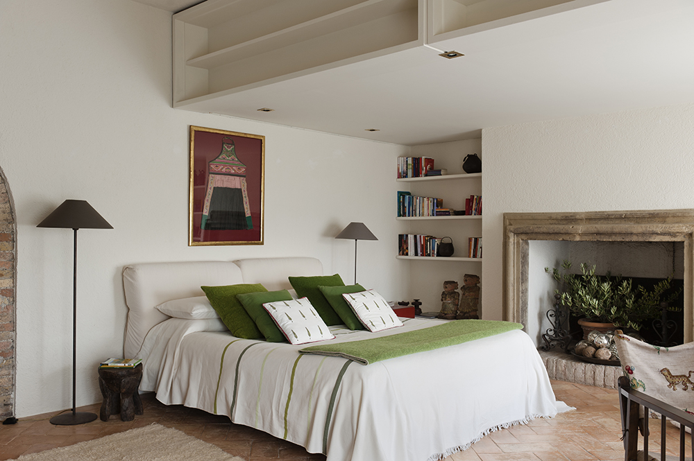 Minimalist white bedroom with fireplace. A potted plant fills the space inside the fireplace.