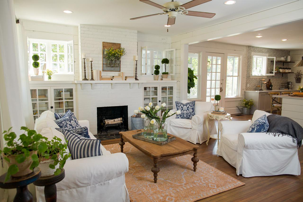 Bright and airy living room with white fireplace and white furniture. Inside the fireplace is a stack of white birch logs.