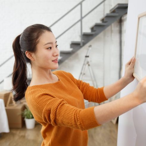 woman hanging framed photo on white wall