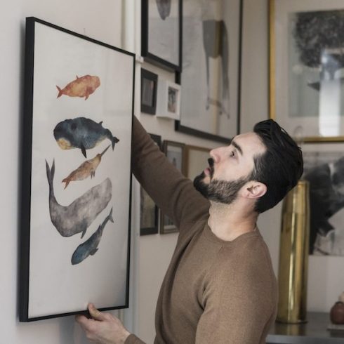 man hanging painting on wall at home