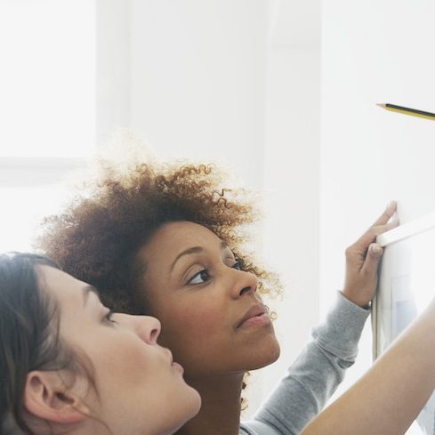 women using level to hang picture on wall