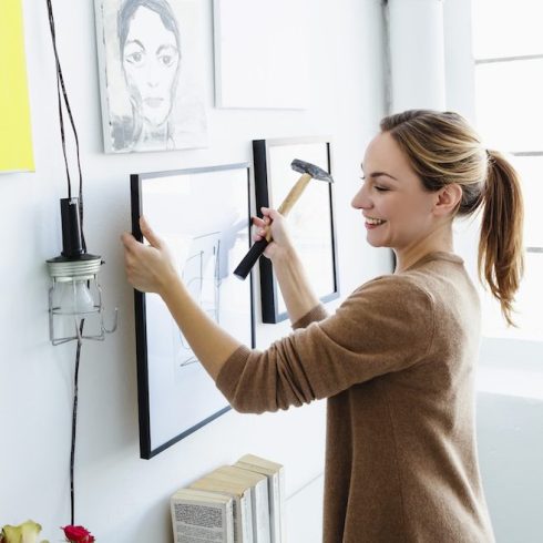 woman holding picture frame and hammer in front of wall